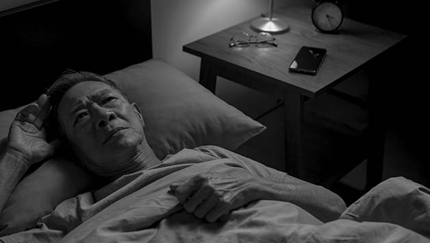 senior man with insomnia lying in bed awake
