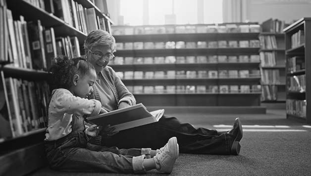 grandma and granddaughter reading book in library